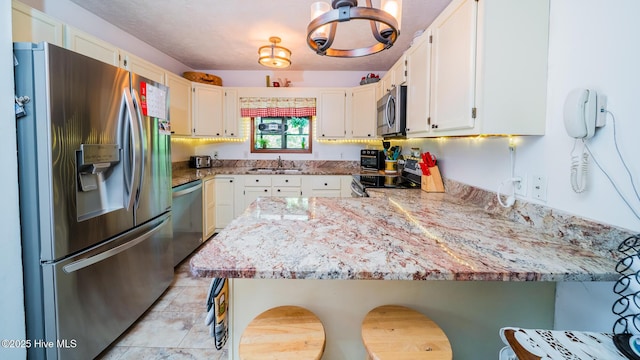 kitchen with a peninsula, a kitchen bar, white cabinetry, a sink, and appliances with stainless steel finishes