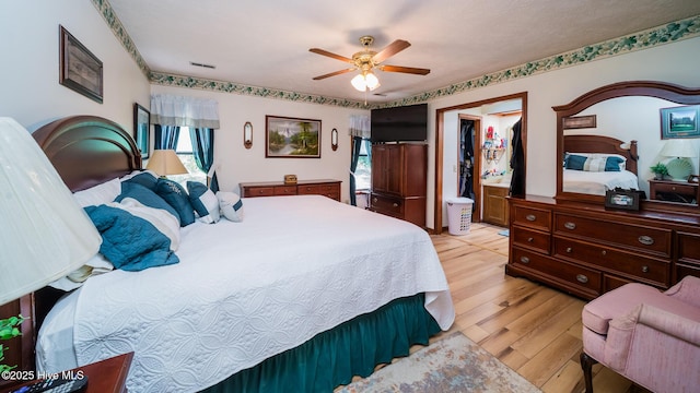 bedroom with light wood-style floors, ceiling fan, and an AC wall unit