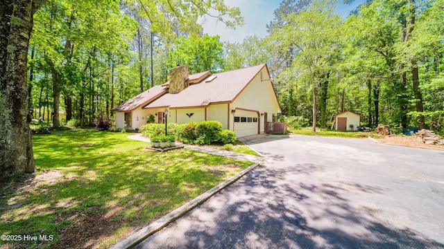 view of home's exterior featuring a garage, driveway, a shed, a chimney, and a yard