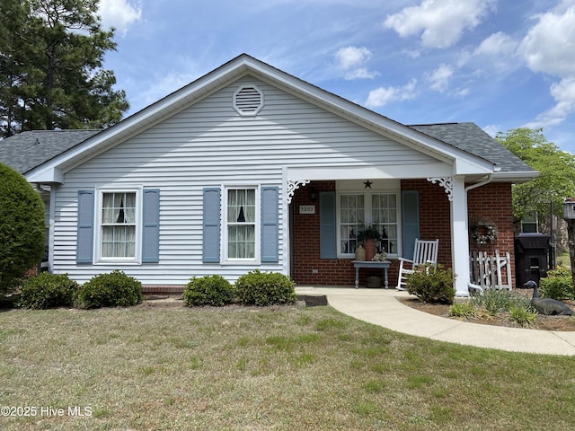 view of front of property with a porch, brick siding, a front yard, and roof with shingles