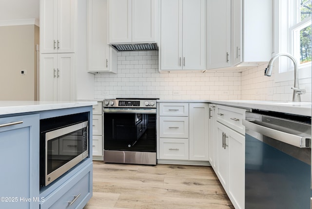 kitchen featuring crown molding, appliances with stainless steel finishes, a sink, light wood-style floors, and decorative backsplash