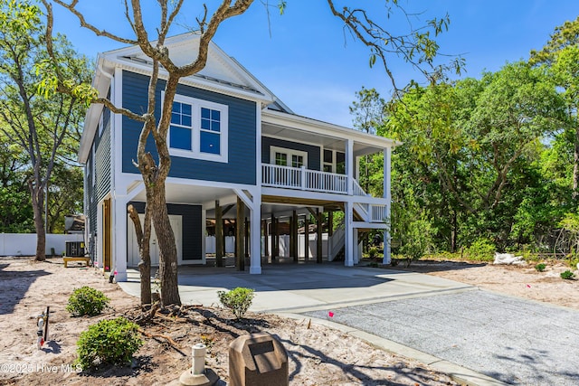 raised beach house featuring concrete driveway, covered porch, and a carport