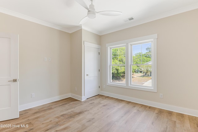 spare room with light wood-style flooring, a ceiling fan, baseboards, visible vents, and ornamental molding