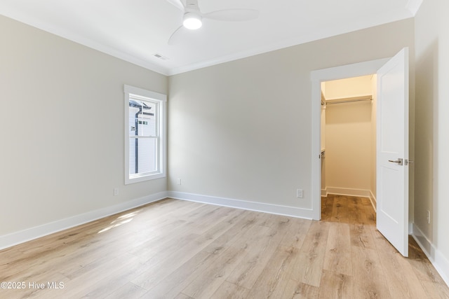 unfurnished bedroom featuring visible vents, ornamental molding, a walk in closet, and light wood-style floors