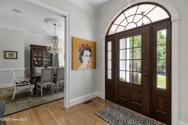 entryway featuring visible vents, baseboards, light wood finished floors, a notable chandelier, and ornamental molding