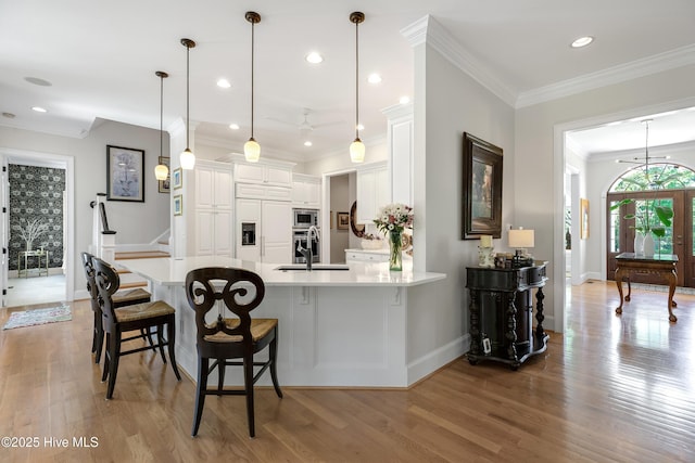 kitchen with built in appliances, a peninsula, baseboards, light wood-type flooring, and a sink