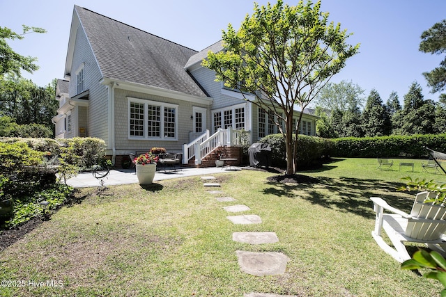 back of property featuring a shingled roof, a yard, and a patio area