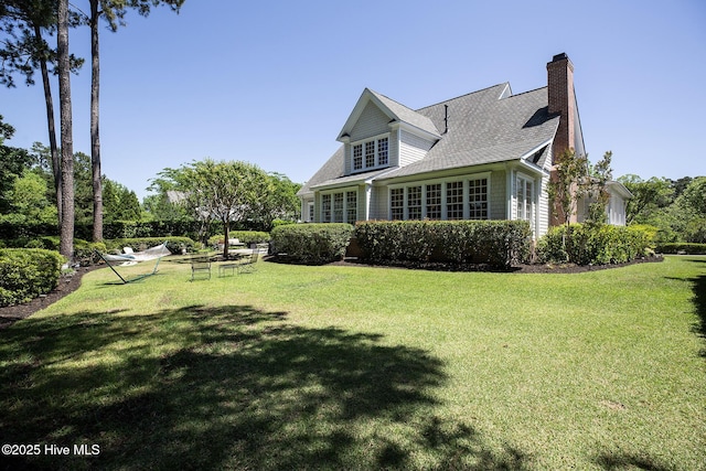 exterior space with a shingled roof, a chimney, and a yard