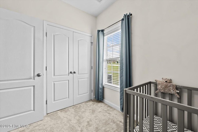 bedroom with a crib, baseboards, light carpet, and a closet