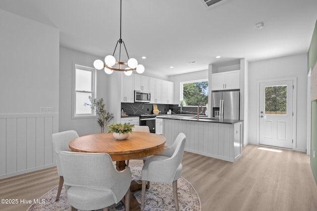 dining area with light wood-style floors, recessed lighting, a wainscoted wall, and a notable chandelier