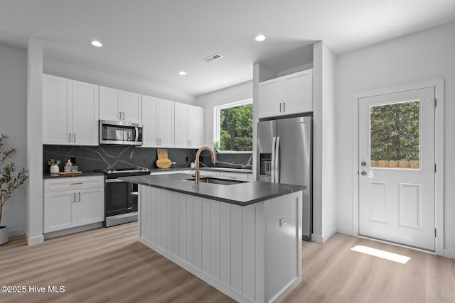 kitchen with dark countertops, a sink, light wood finished floors, stainless steel appliances, and visible vents