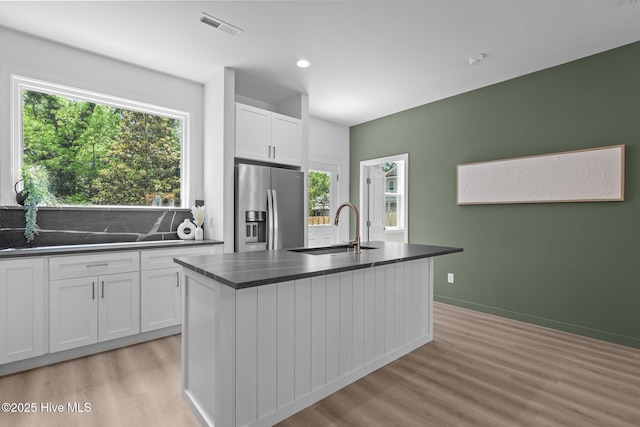 kitchen featuring a sink, stainless steel fridge with ice dispenser, light wood-type flooring, and dark countertops