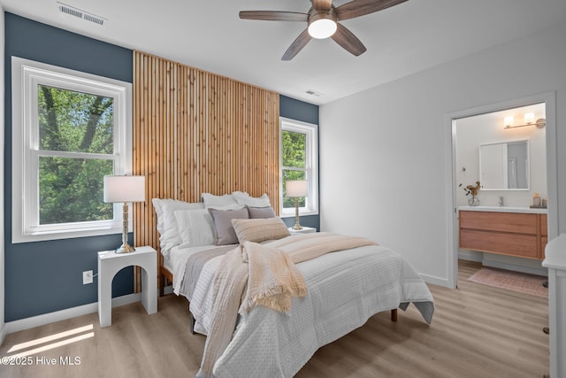 bedroom featuring baseboards, visible vents, light wood-style flooring, and ensuite bath