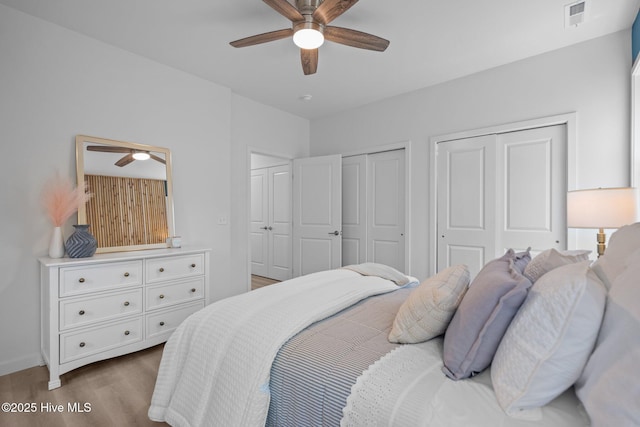bedroom with visible vents, two closets, wood finished floors, baseboards, and ceiling fan