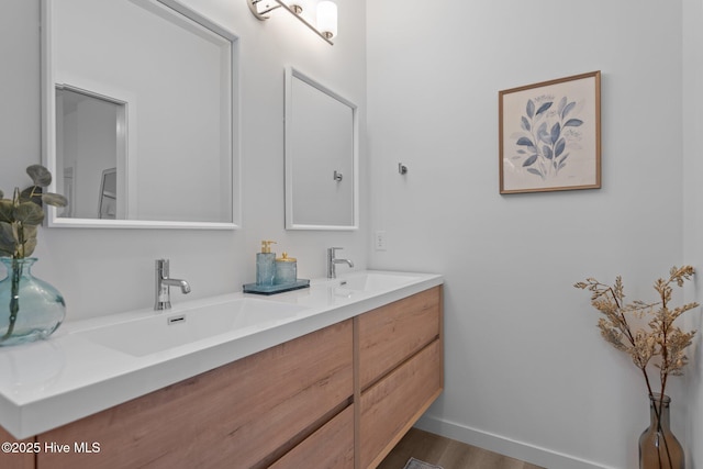 full bathroom featuring double vanity, a sink, baseboards, and wood finished floors