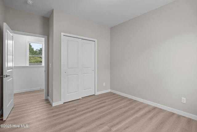 unfurnished bedroom featuring baseboards, light wood-style flooring, and a closet