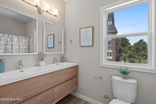 full bath featuring double vanity, toilet, baseboards, and a sink