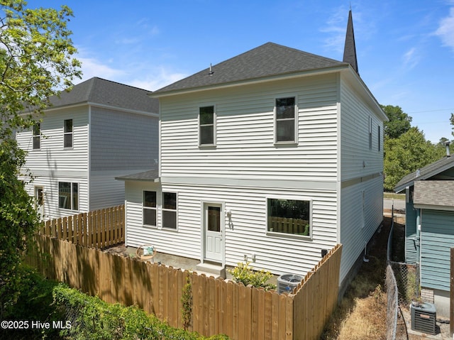 rear view of property featuring fence, central AC, and roof with shingles