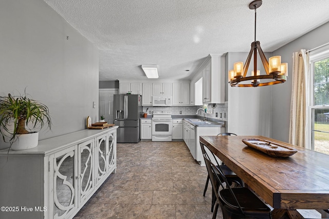 kitchen featuring white appliances, stone finish floor, a textured ceiling, a chandelier, and white cabinets