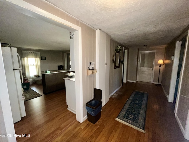 hallway with baseboards, a textured ceiling, and wood finished floors