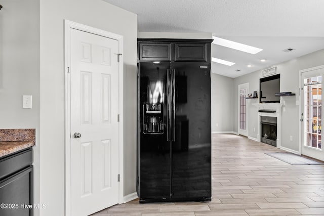 kitchen featuring light stone counters, black fridge, light wood finished floors, baseboards, and a skylight