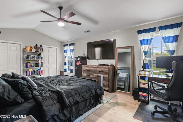 bedroom featuring ceiling fan, two closets, wood finished floors, vaulted ceiling, and visible vents