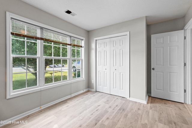 unfurnished bedroom featuring light wood-type flooring, baseboards, visible vents, and a closet