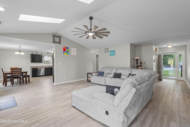 living room featuring baseboards, ceiling fan with notable chandelier, vaulted ceiling with skylight, and light wood-style floors