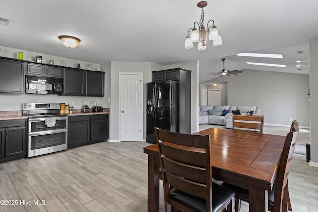dining space with baseboards, ceiling fan with notable chandelier, light wood finished floors, and lofted ceiling with skylight