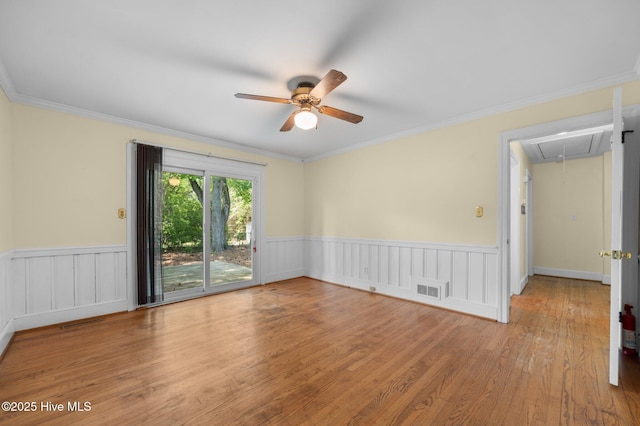 spare room with a ceiling fan, attic access, visible vents, wainscoting, and wood finished floors