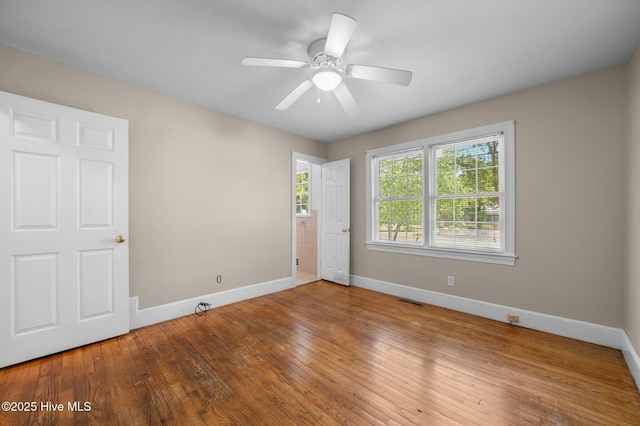 empty room with baseboards, a ceiling fan, hardwood / wood-style floors, and visible vents