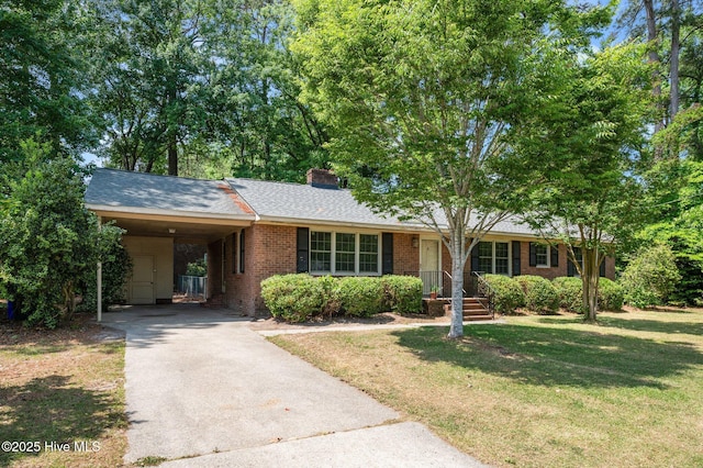 ranch-style house featuring a front yard, an attached carport, a chimney, brick siding, and driveway