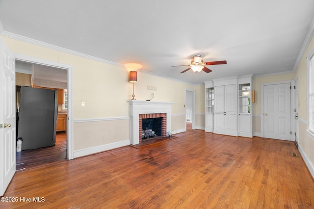 unfurnished living room featuring ornamental molding, a fireplace, a ceiling fan, and wood finished floors