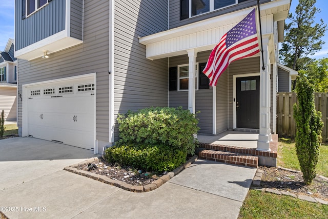 view of exterior entry featuring a porch, fence, an attached garage, and driveway