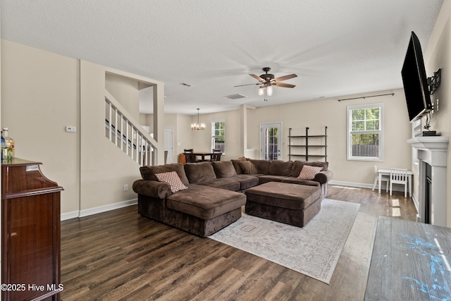 living area featuring visible vents, a fireplace with flush hearth, wood finished floors, ceiling fan with notable chandelier, and stairs