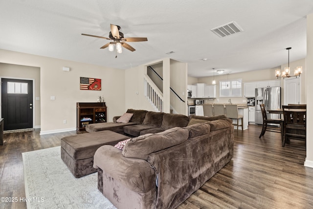 living room with a wealth of natural light, ceiling fan with notable chandelier, dark wood finished floors, and visible vents