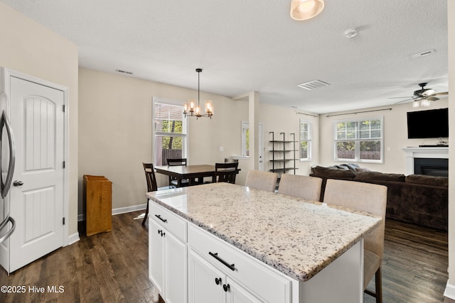 kitchen with a glass covered fireplace, dark wood-type flooring, ceiling fan with notable chandelier, and visible vents