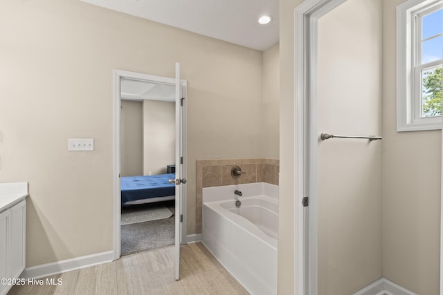 bathroom featuring a bath, wood finished floors, vanity, baseboards, and ensuite bathroom