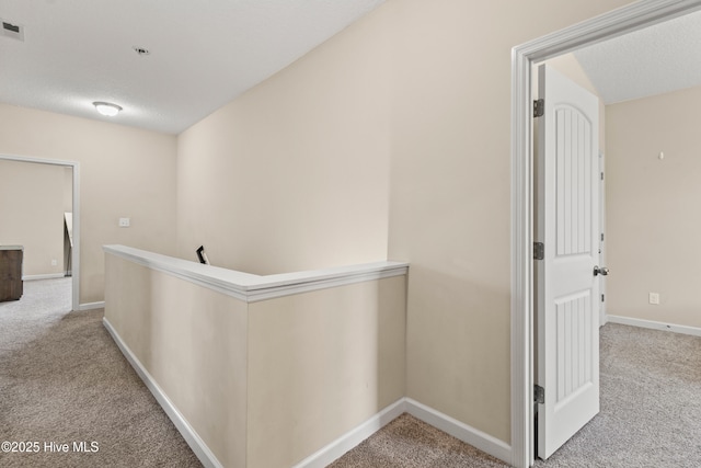 hall featuring carpet floors, baseboards, and an upstairs landing