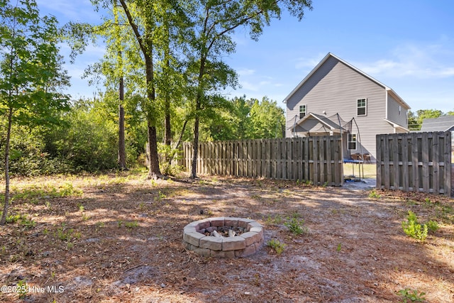 view of yard with fence, a trampoline, and an outdoor fire pit