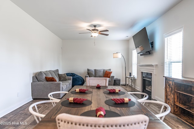 dining room with baseboards, a ceiling fan, a glass covered fireplace, and wood finished floors