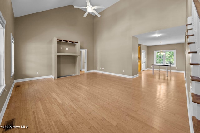unfurnished living room featuring visible vents, light wood finished floors, ceiling fan with notable chandelier, and high vaulted ceiling