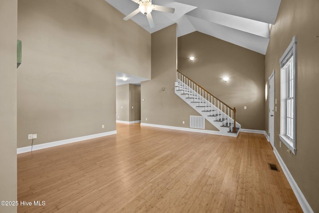 unfurnished living room with visible vents, ceiling fan, high vaulted ceiling, and stairway
