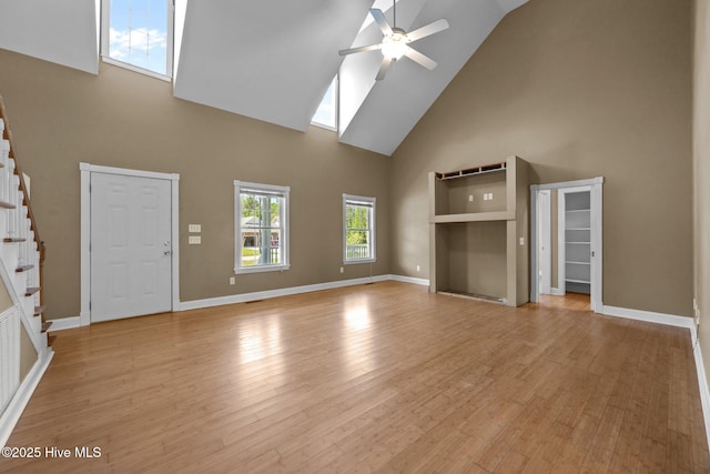 unfurnished living room with ceiling fan, light wood-type flooring, stairway, high vaulted ceiling, and baseboards