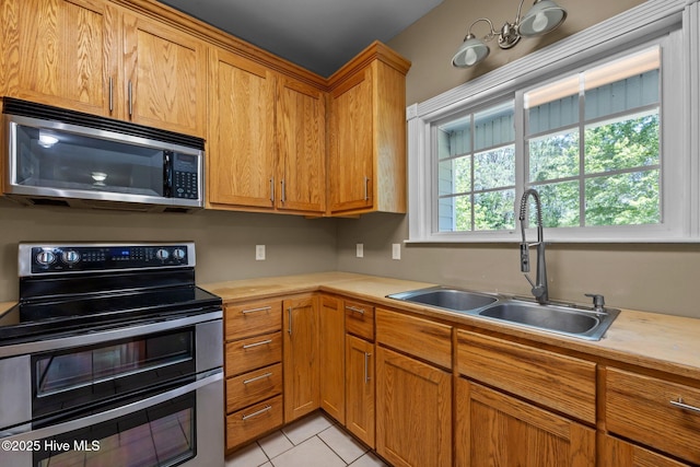 kitchen with light tile patterned floors, appliances with stainless steel finishes, brown cabinetry, and a sink