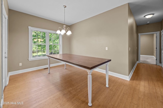 unfurnished dining area featuring baseboards, a chandelier, and light wood-type flooring