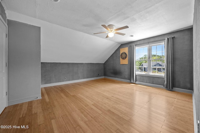 additional living space featuring a textured ceiling, ceiling fan, vaulted ceiling, and wood finished floors