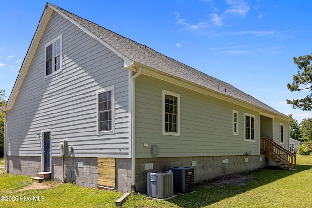 back of property with roof with shingles, central AC, and a yard