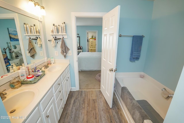ensuite bathroom featuring a garden tub, a sink, connected bathroom, and wood finished floors