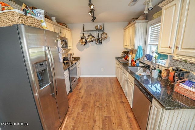 kitchen with backsplash, appliances with stainless steel finishes, a sink, baseboards, and light wood-style flooring